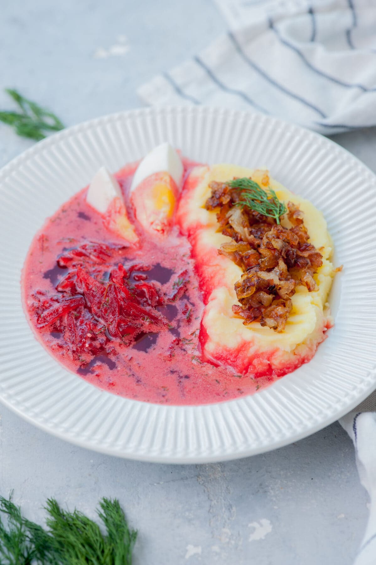 Barszcz soup in a white plate with mashed potatoed and onion bacon topping.
