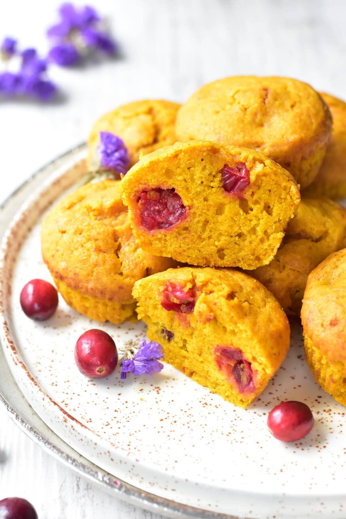 Pumpkin cranberry muffins on a white plate. Two muffins are cut in half.