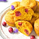 Pumpkin cranberry muffins on a white plate. Two muffins cut in half.