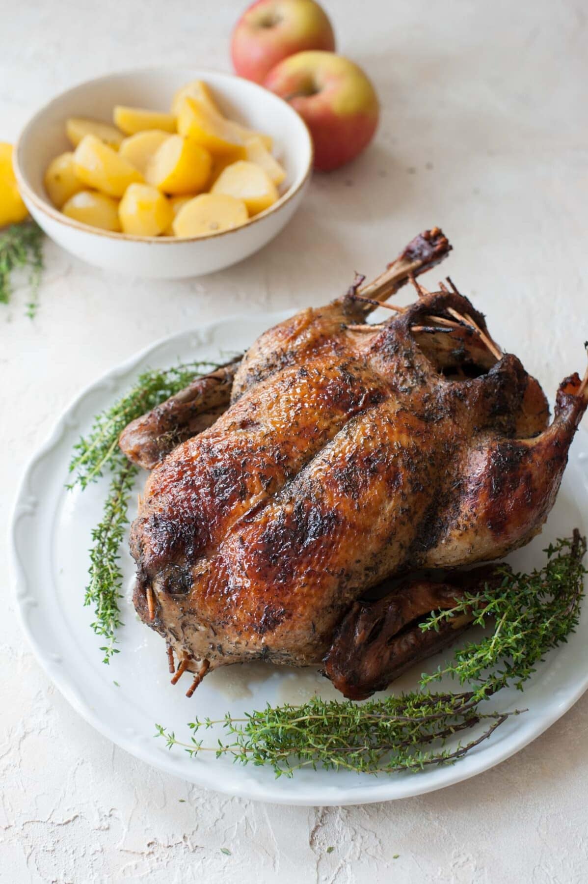 Roast duck on a white plate. Potatoes and apples in the background.