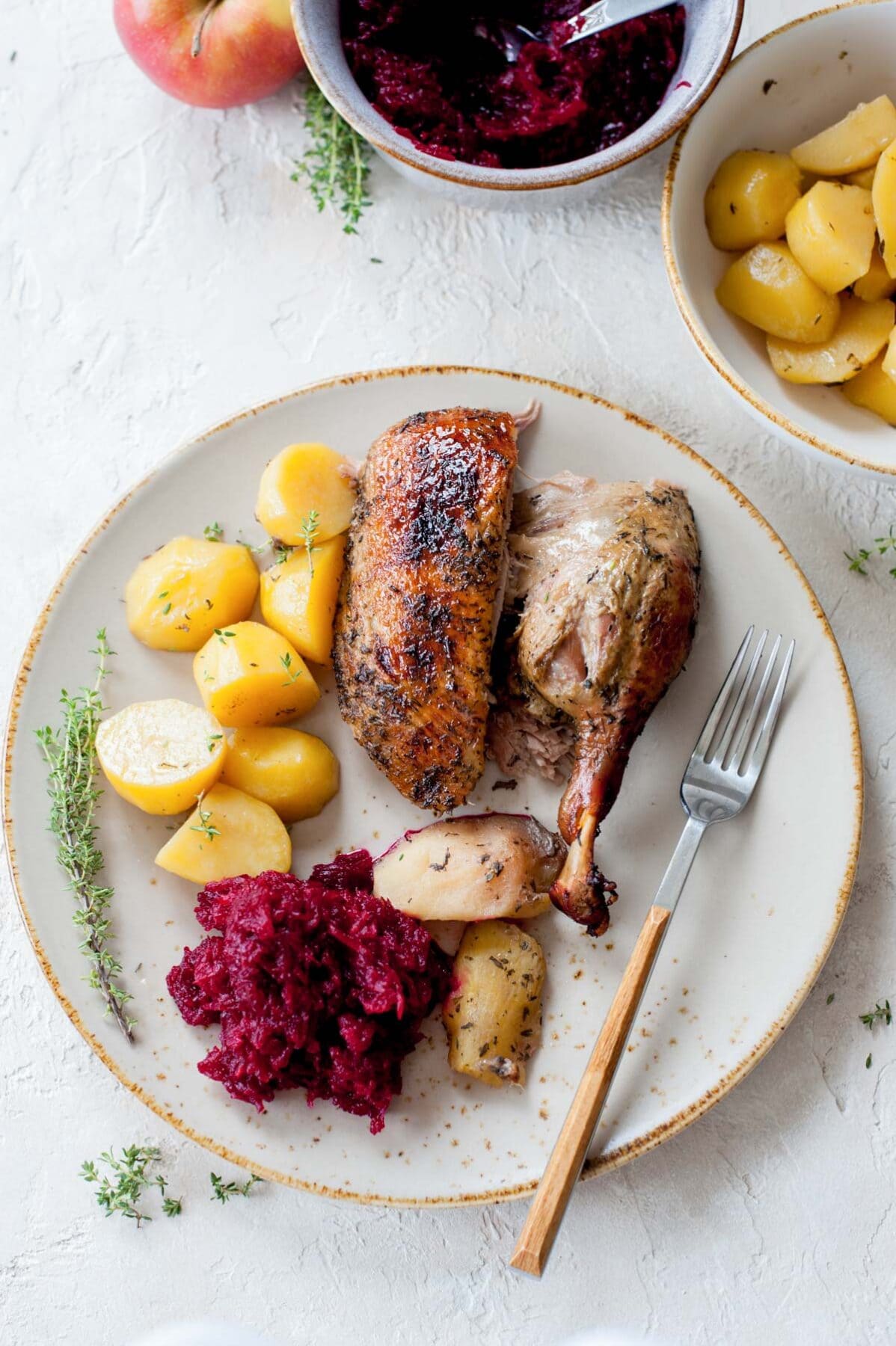 Roasted duck breast and leg, potatoes, apples, and beet salad on a beige plate.