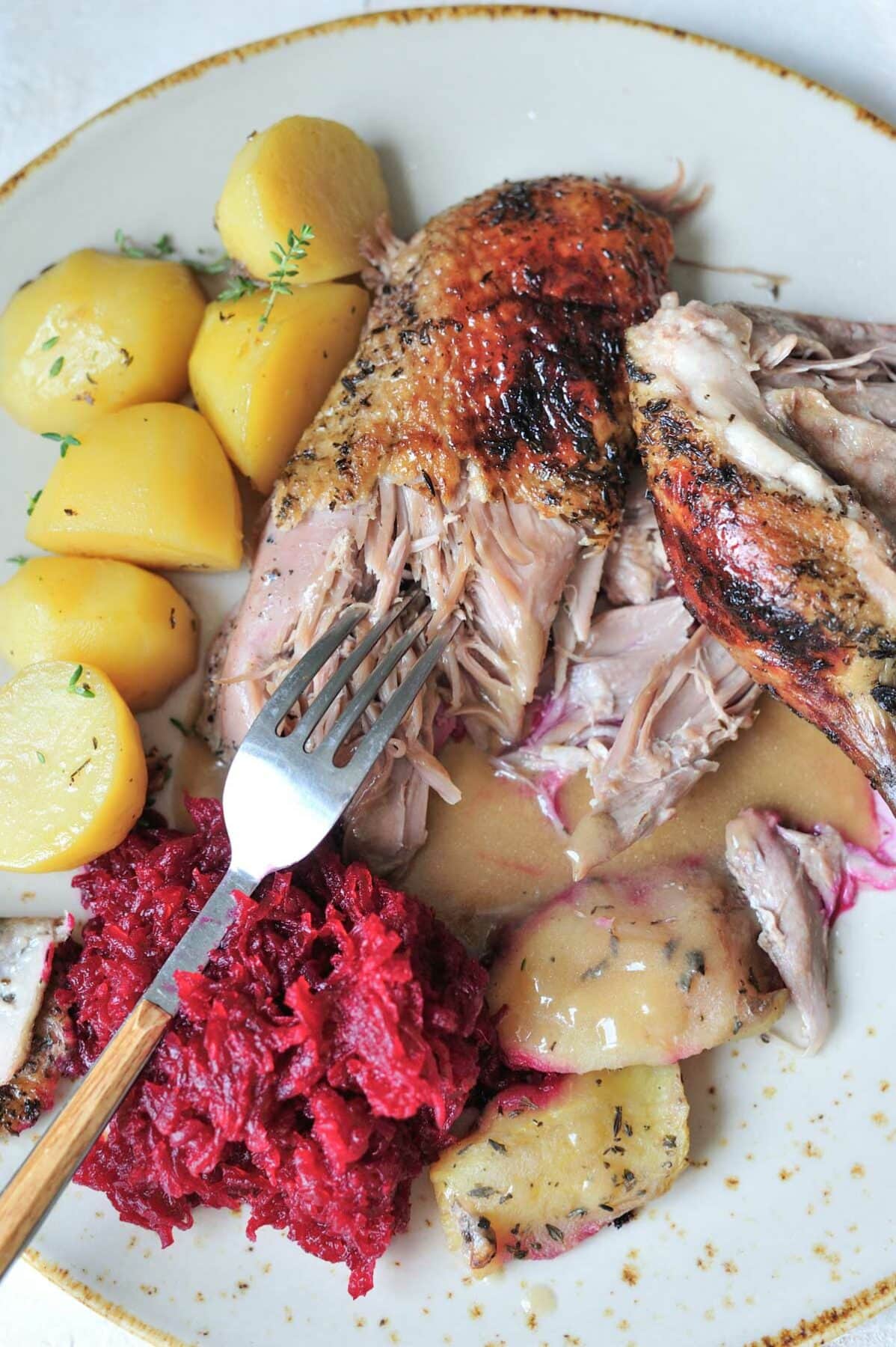 Duck breast on a plate is being cut with a fork.