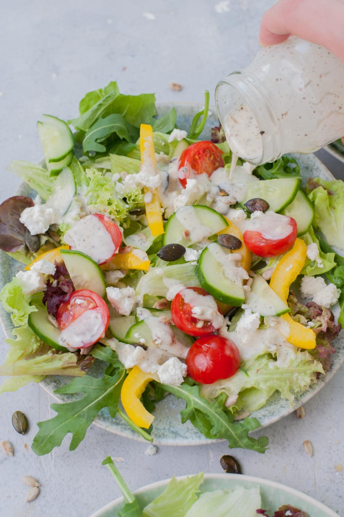 Yogurt dressing is being poured over lettuce and veggies on a green plate.