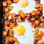 Sweet potato breakfast hash with eggs on a black baking sheet.