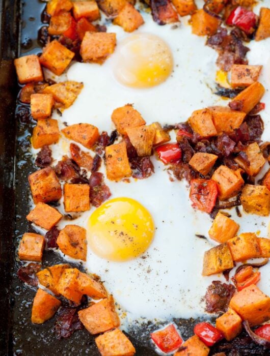 Sweet potato breakfast hash with eggs on a black baking sheet.