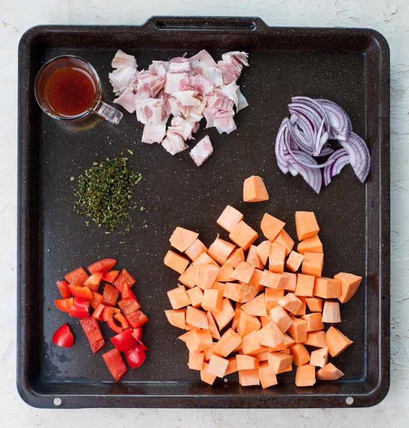 Chopped ingredients for sweet potato breakfast hash on a black baking sheet.