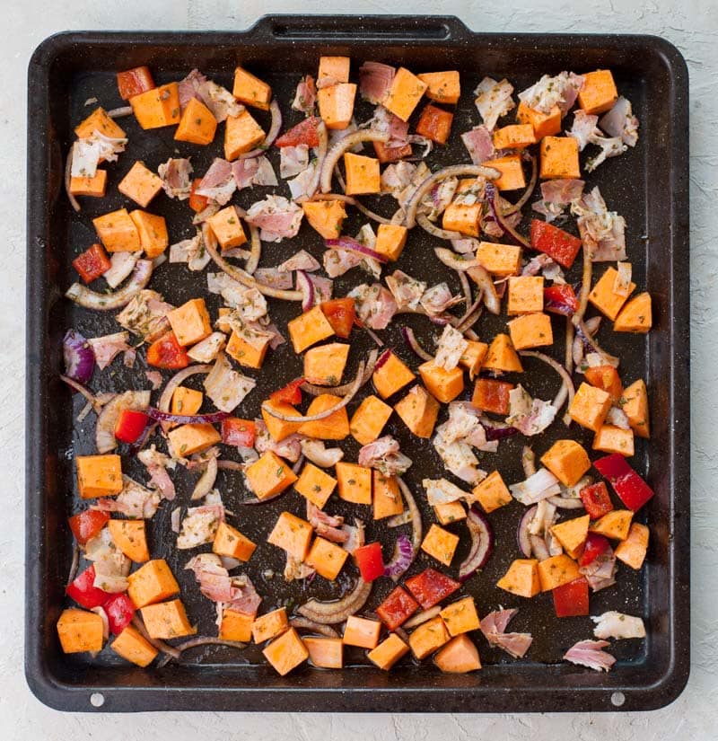 Chopped ingredients mixed together for sweet potato breakfast hash on a black baking sheet.