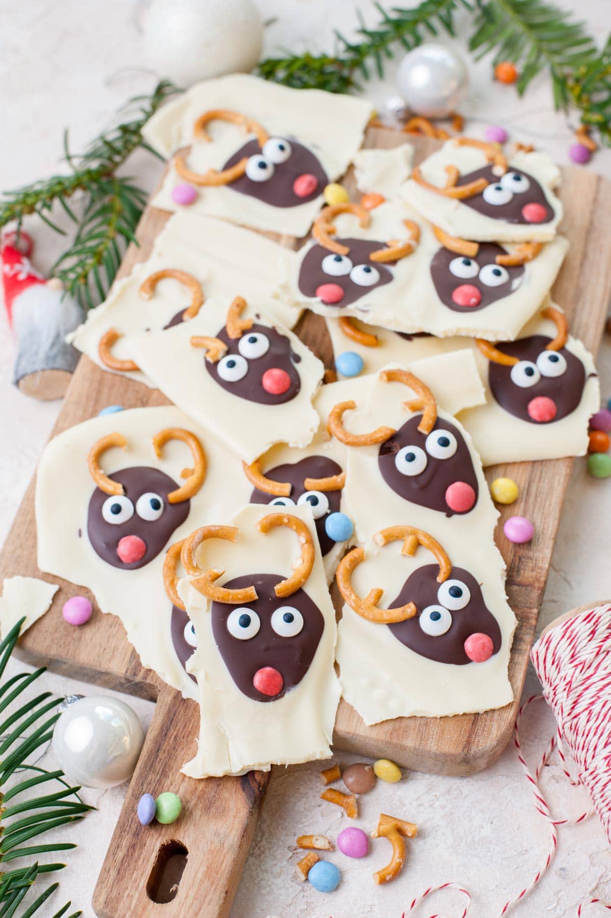 Broken into pieces Christmas bark with chocolate reindeer faces on a wooden board.