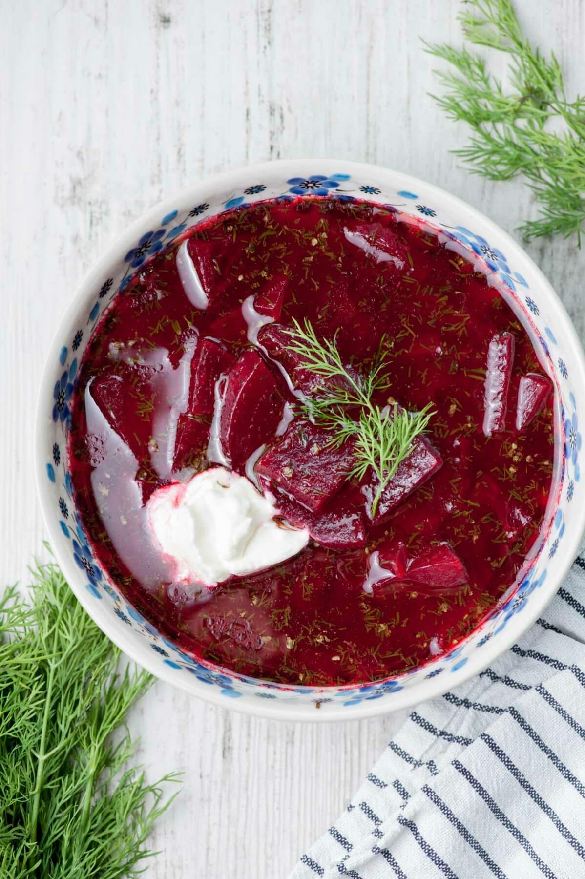 Beet soup in a white-blue plate topped with sour cream and fresh dill.