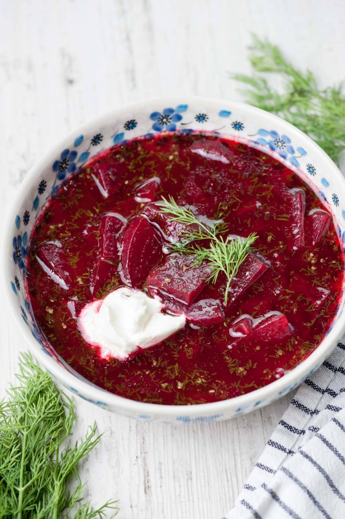 Beet soup in a white-blue plate topped with sour cream and dill.