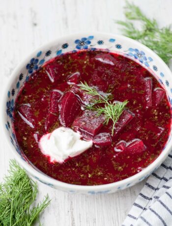 Beet soup in a white-blue plate topped with sour cream and dill.