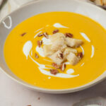 Butternut squash soup in a beige bowl topped with cheese croutons and pecans.