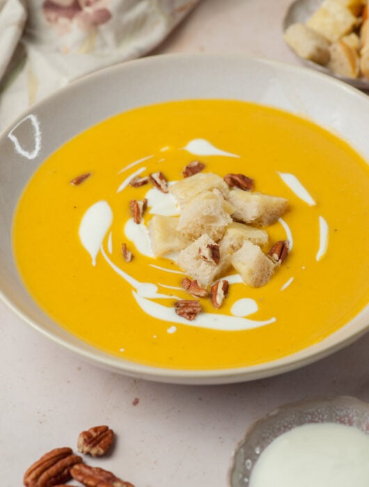 Butternut squash soup in a beige bowl topped with cheese croutons and pecans.