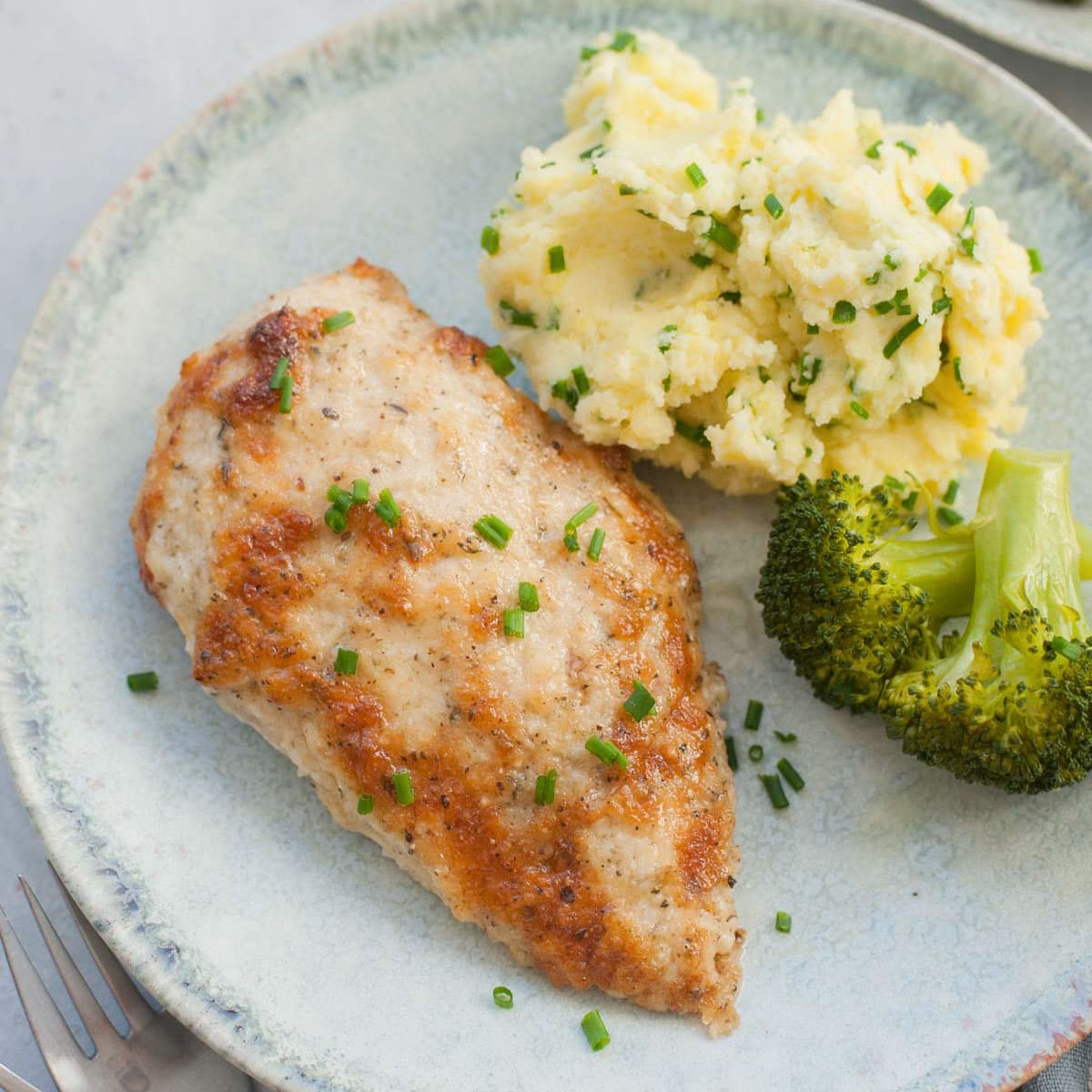 Baked chicken breast on a green plate with mashed potatoes and broccoli.