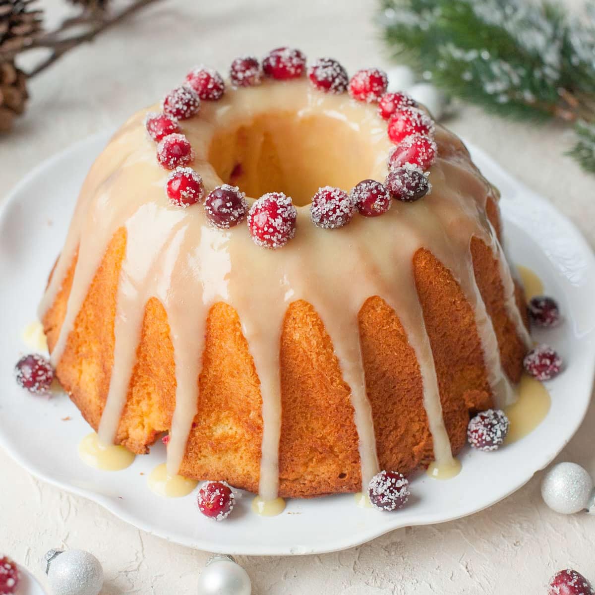 Cranberry orange bundt cake decorated with sugared cranberries on a white plate.