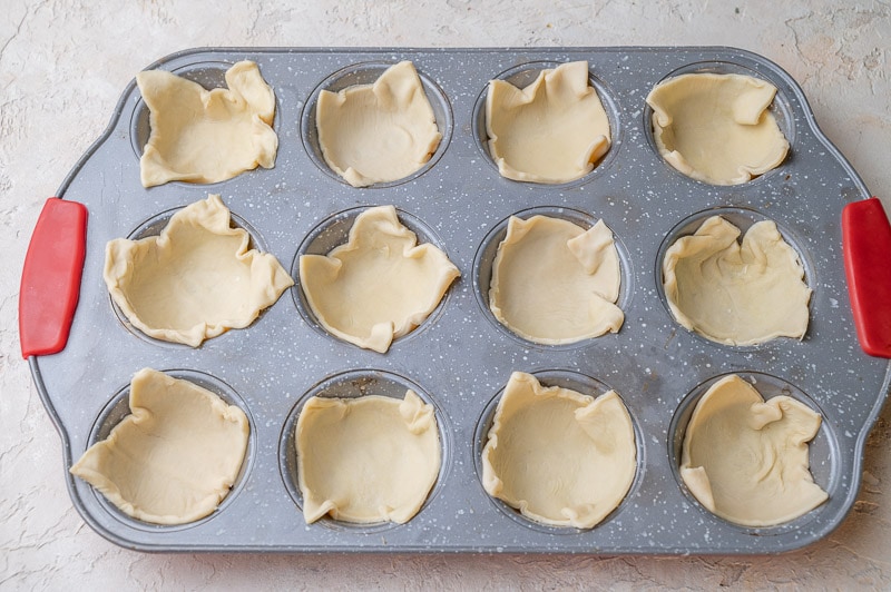 Squares of puff pastry in a muffin tray.