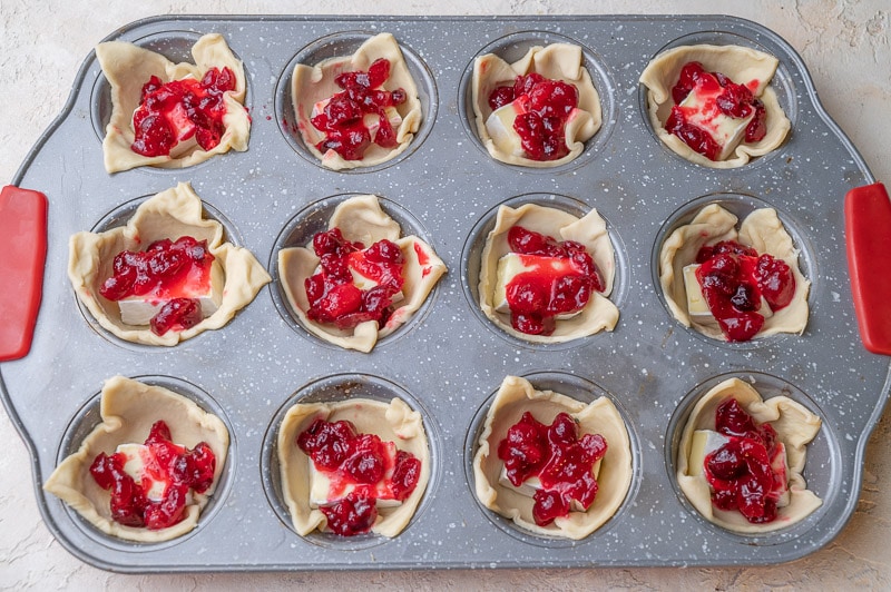 Puff pastry squares in a muffin tray with cubes of brie cheese and cranberry sauce.