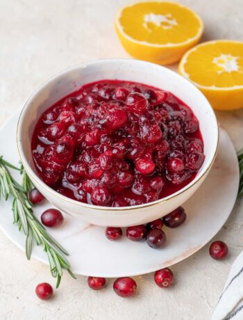 Cranberry orange sauce in a white bowl. Oranges and rosemary twigs in the background.