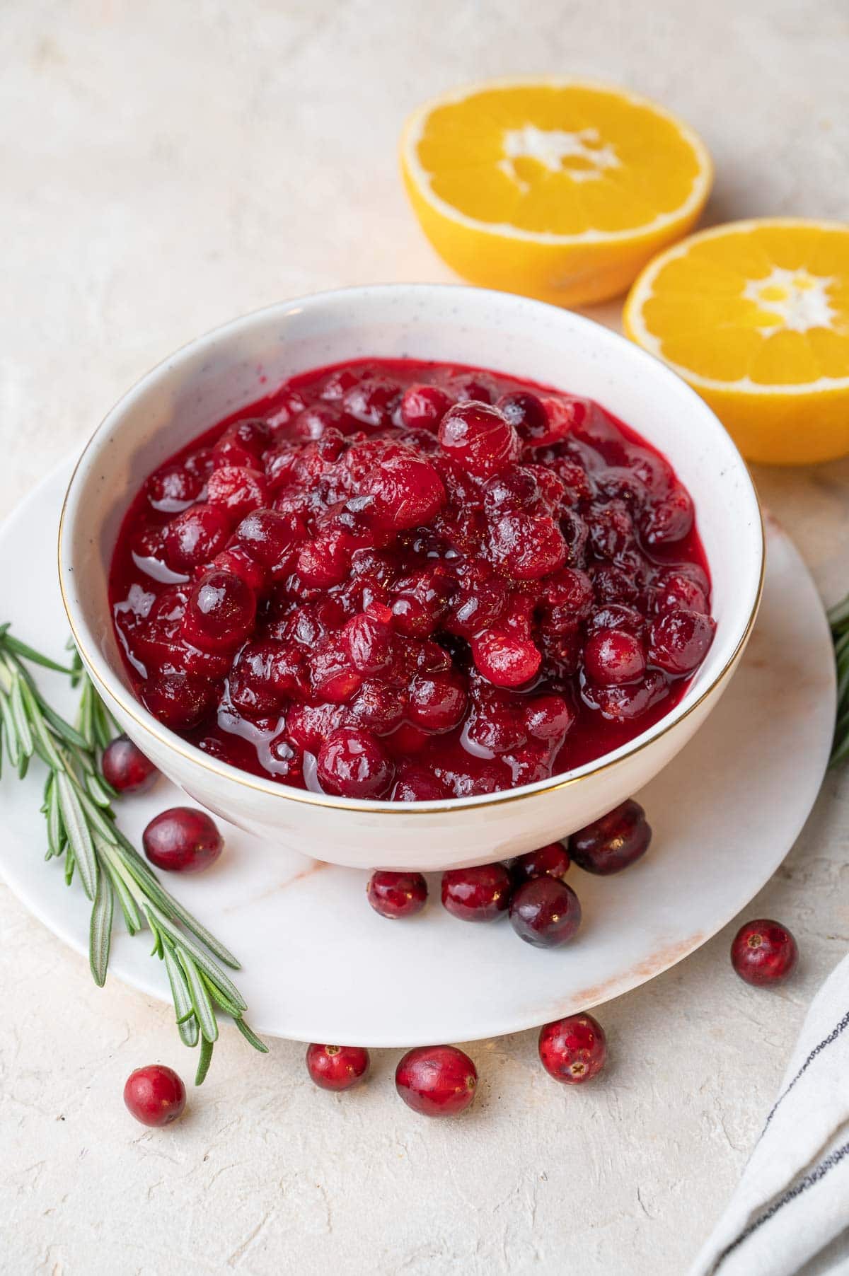 Cranberry orange sauce in a white bowl. Oranges and rosemary twigs in the background.