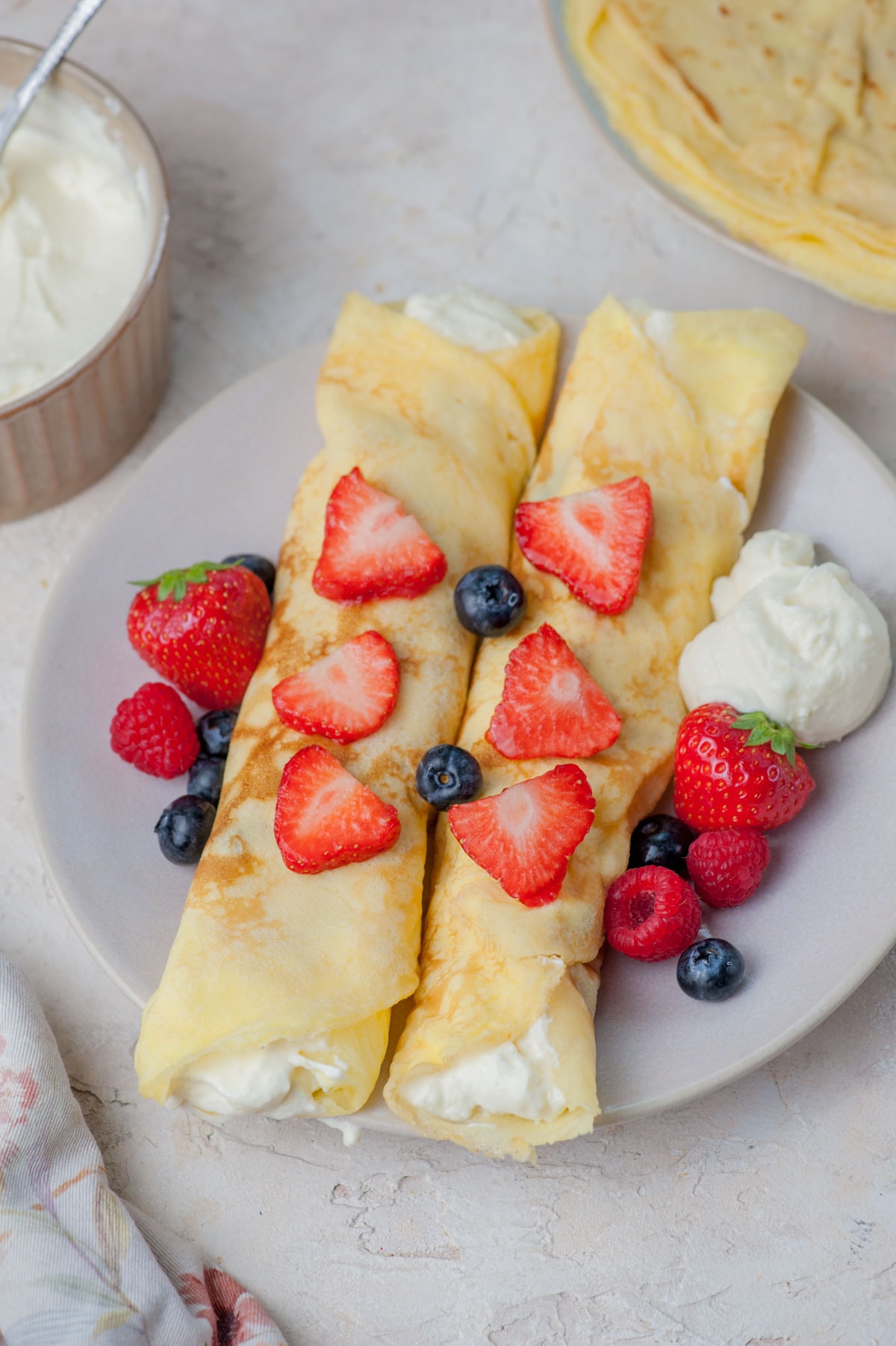 Rolled up creped filled with cream cheese filling and topped with berries on a plate.