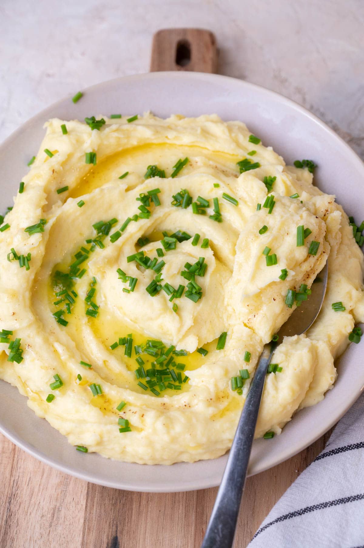 Cream cheese mashed potatoes in a beige bowl topped with chives, a spoon on the side.