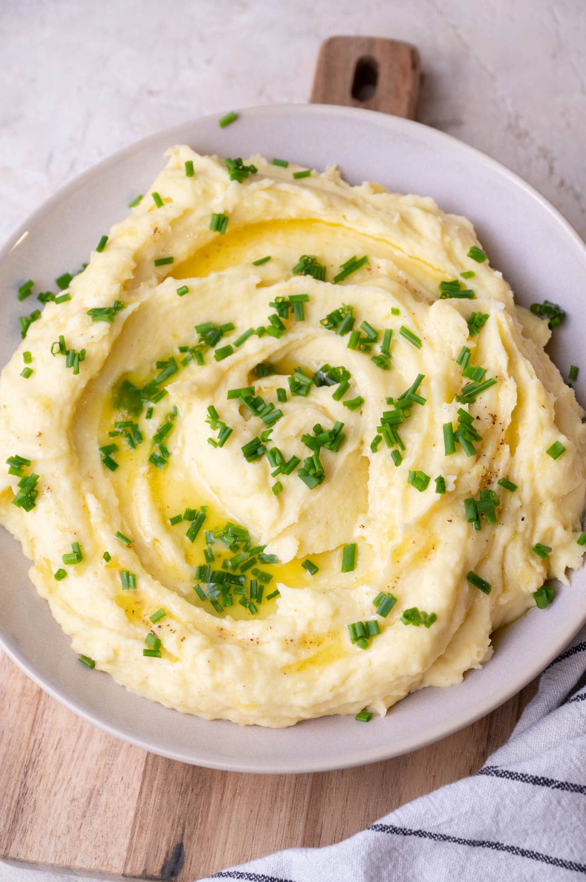 Cream cheese mashed potatoes in a beige bowl topped with chives.