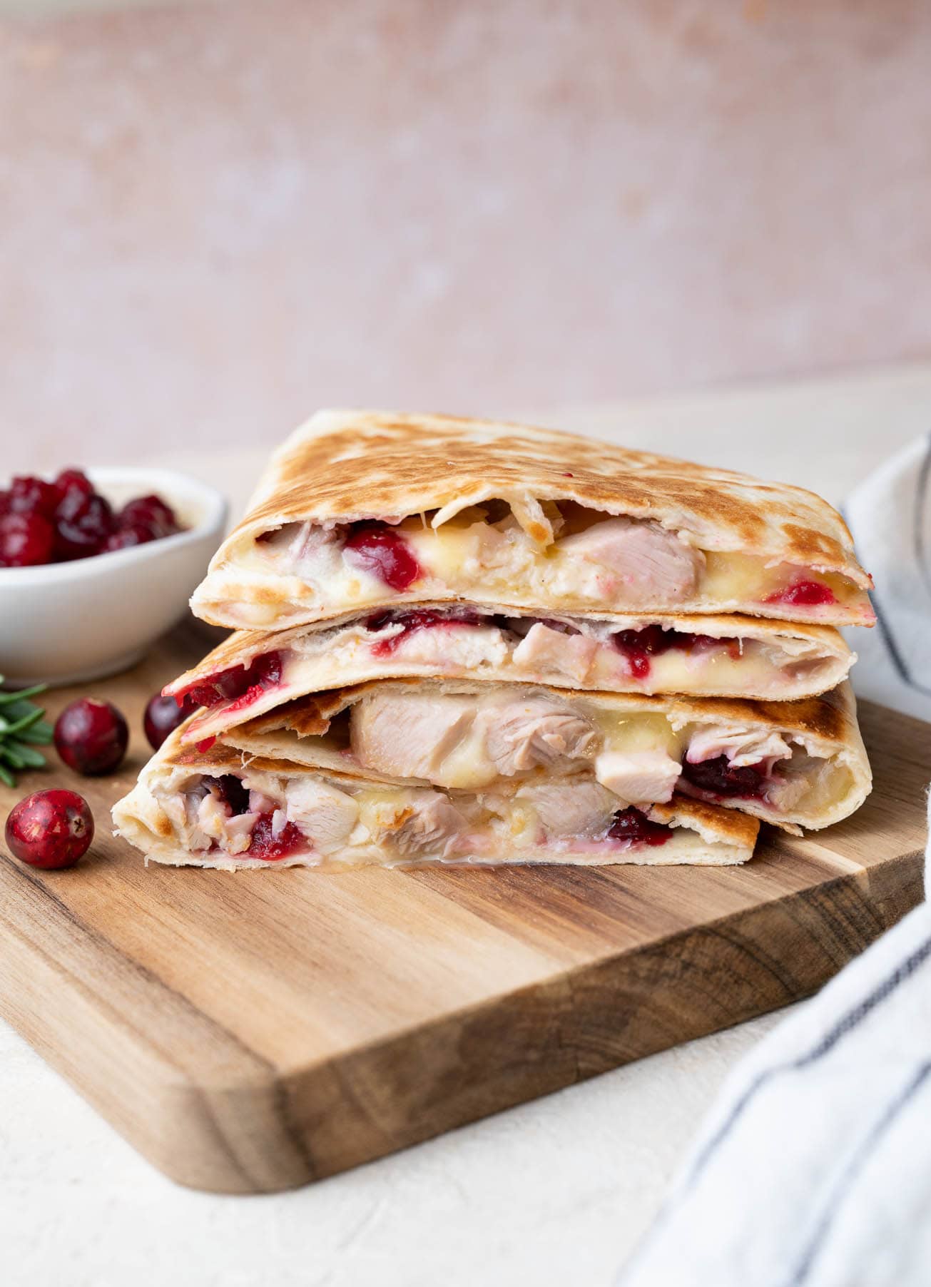 A stack of turkey quesadillas on a wooden board. Fresh cranberries and cranberry sauce in the background.