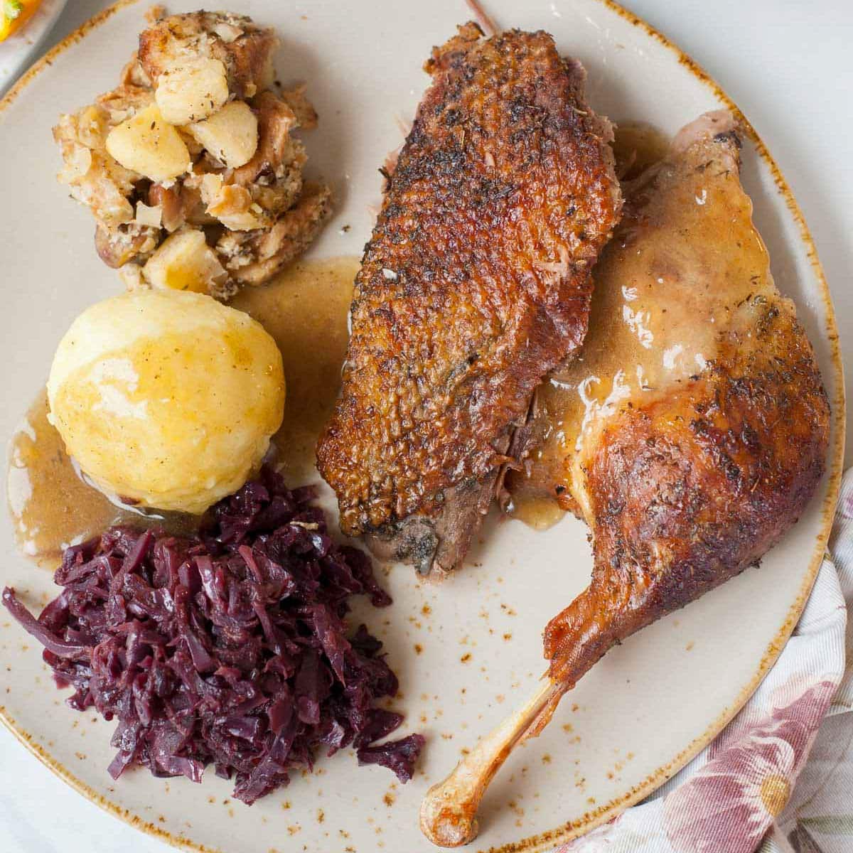 Roast goose with red cabbage and potato dumplings on a light brown plate.