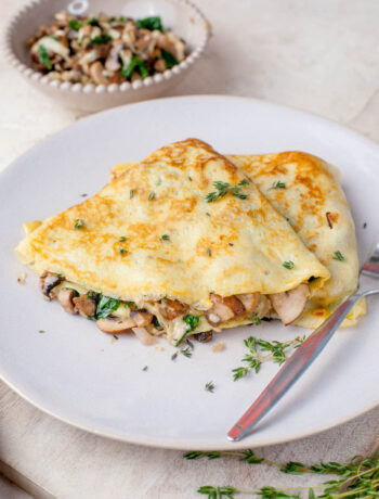 Two mushroom filled crepes on a beige plate with a fork on the side.