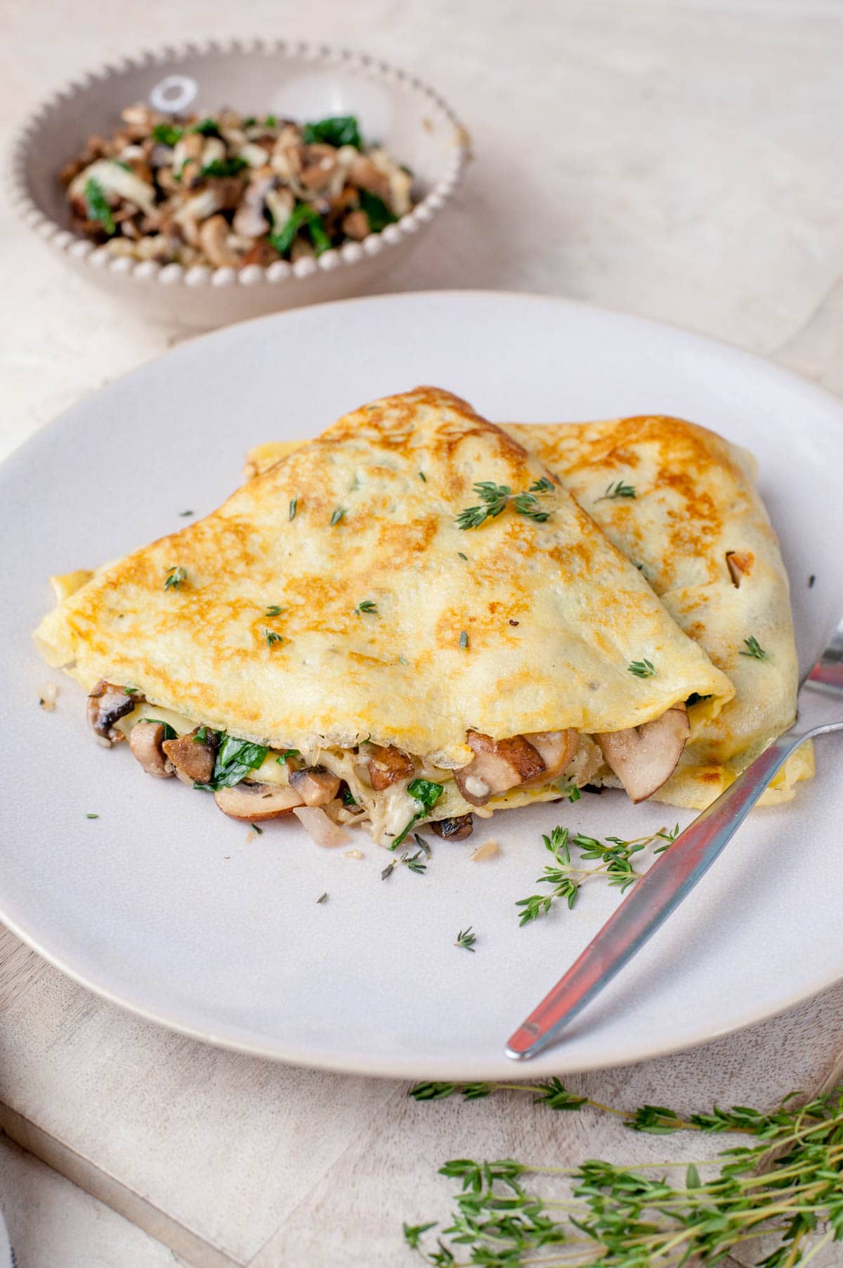 Two mushroom crepes on a beige plate with a fork on the side.