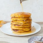 A stack of pumpkin pancakes is being poured with maple syrup.