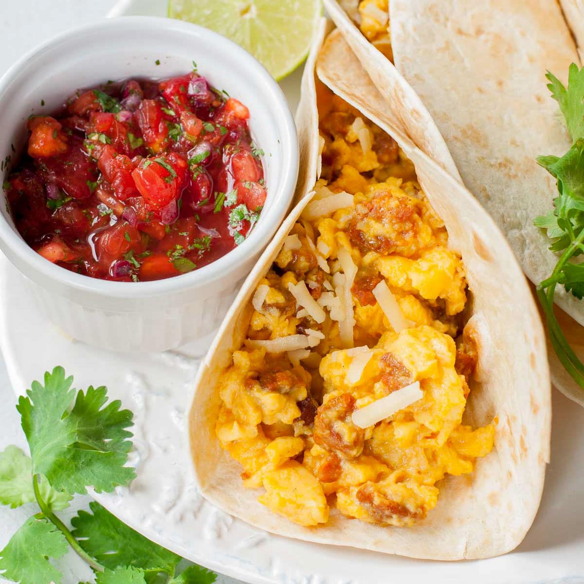 Scrambled eggs tacos with pico de gallo on a white plate.