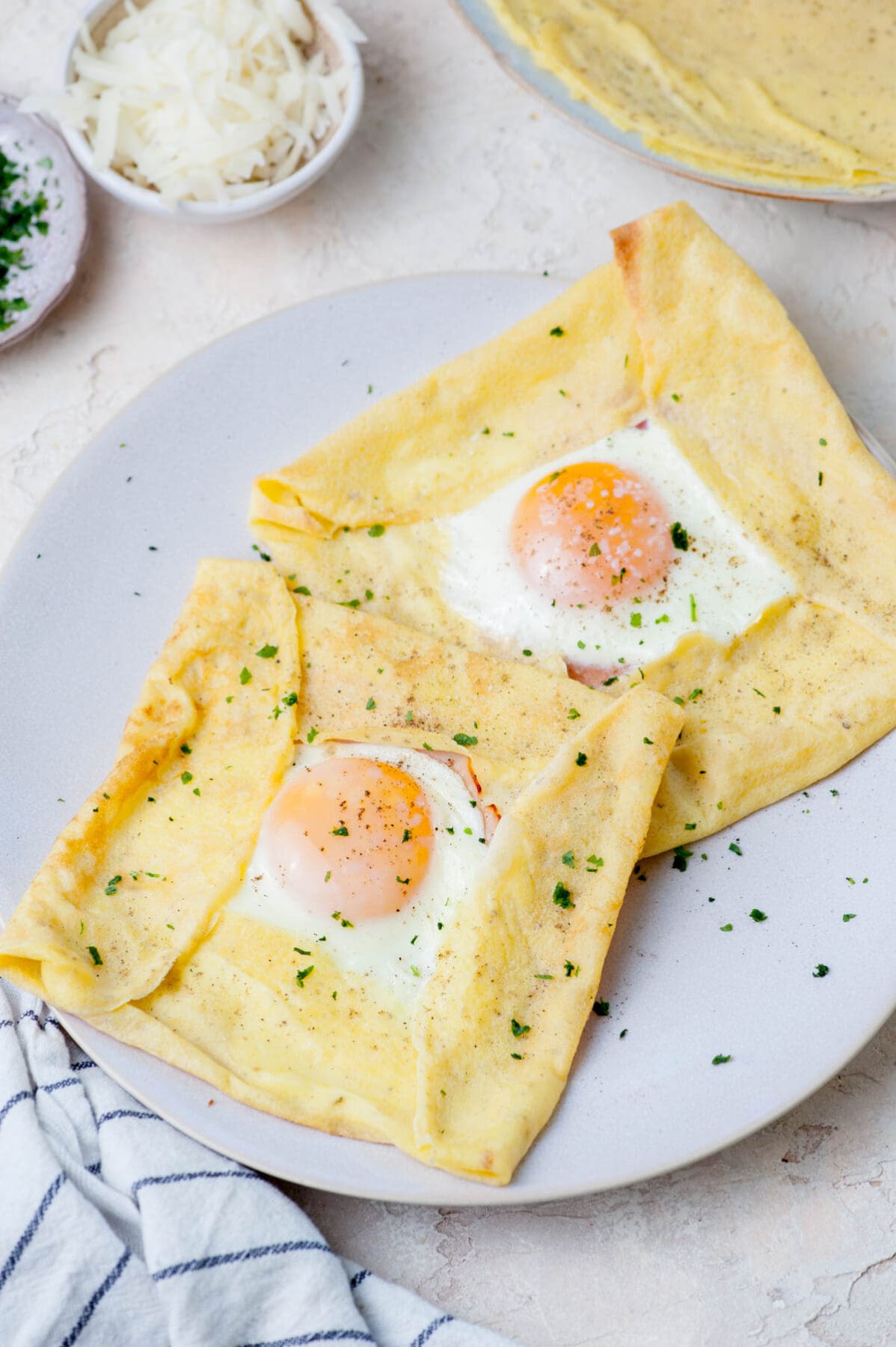 Two crepes with ham, cheese, and eggs on a beige plate.