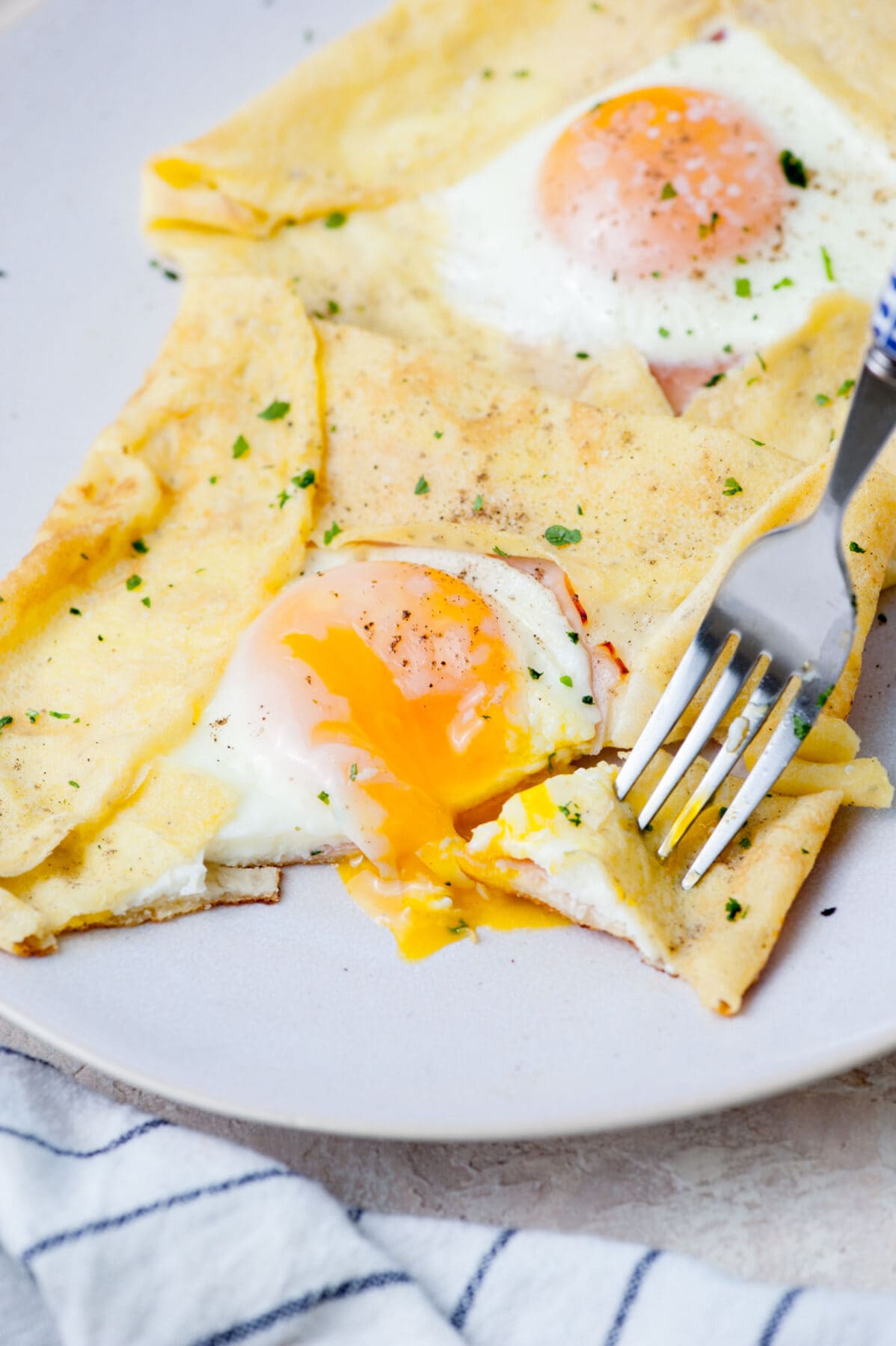 A savory crepe with egg, ham, and cheese is being stuck on a fork.