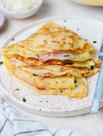 Savory crepes with cheese, ham, and eggs on a white plate.