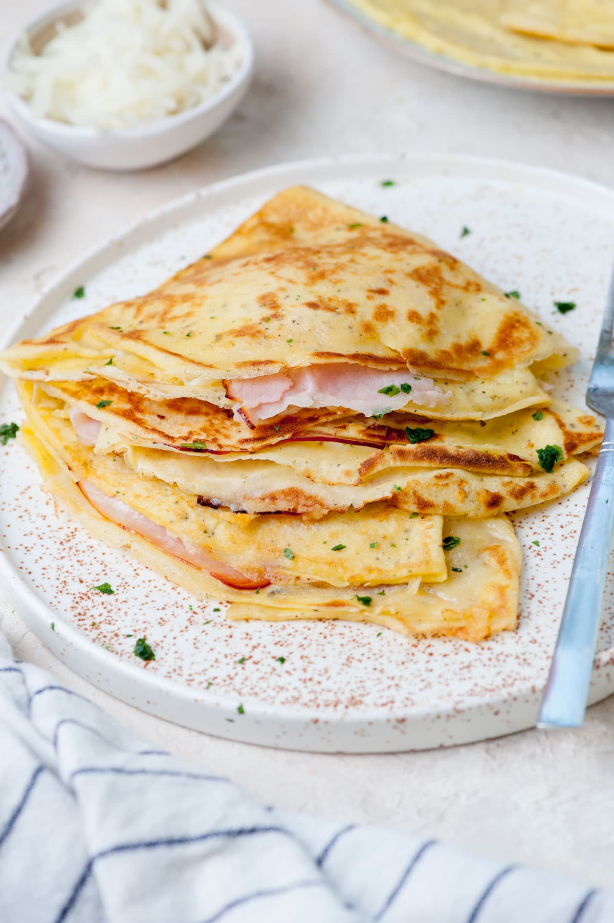 Savory crepes with cheese, ham, and eggs on a white plate.