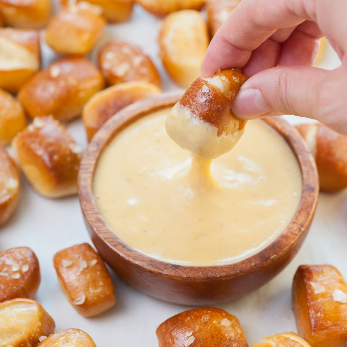 Pretzel bites are being dipped in cheese sauce.