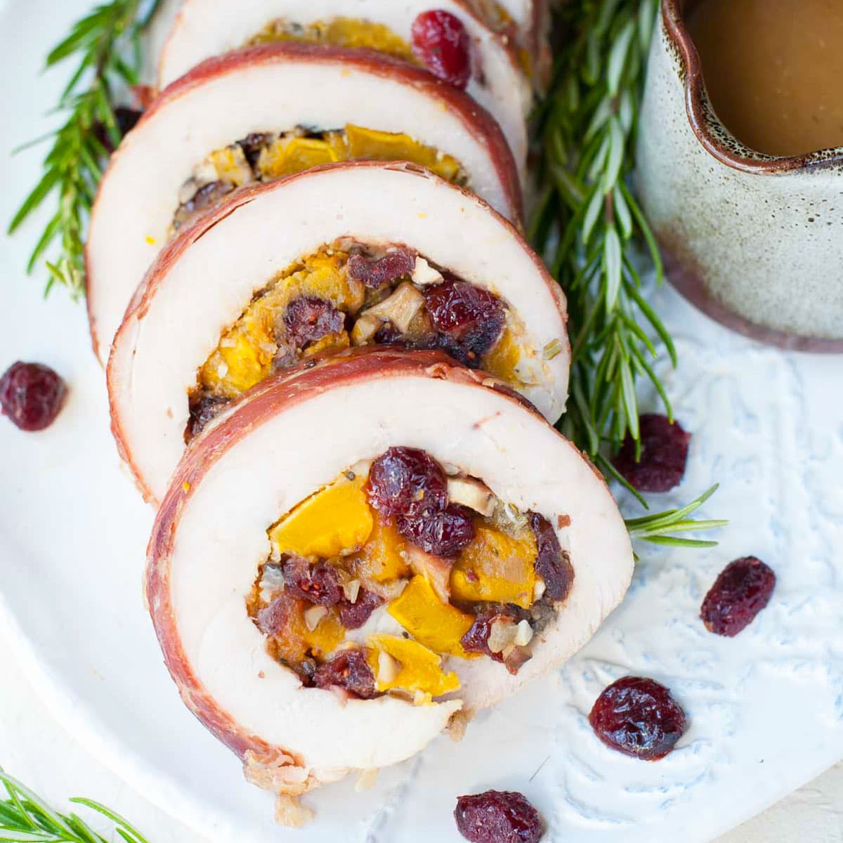 Turkey roulade stuffed with butternut squash and cranberries on a white plate.