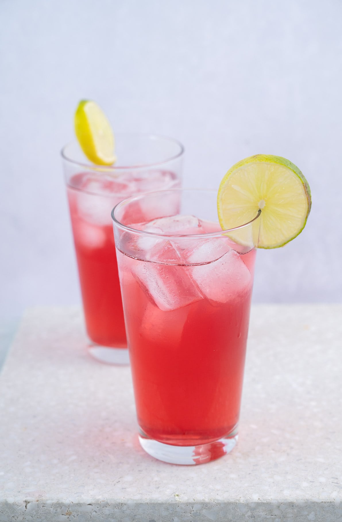 Two glasses with bay breeze drink garnished with lime slices on a stone board.