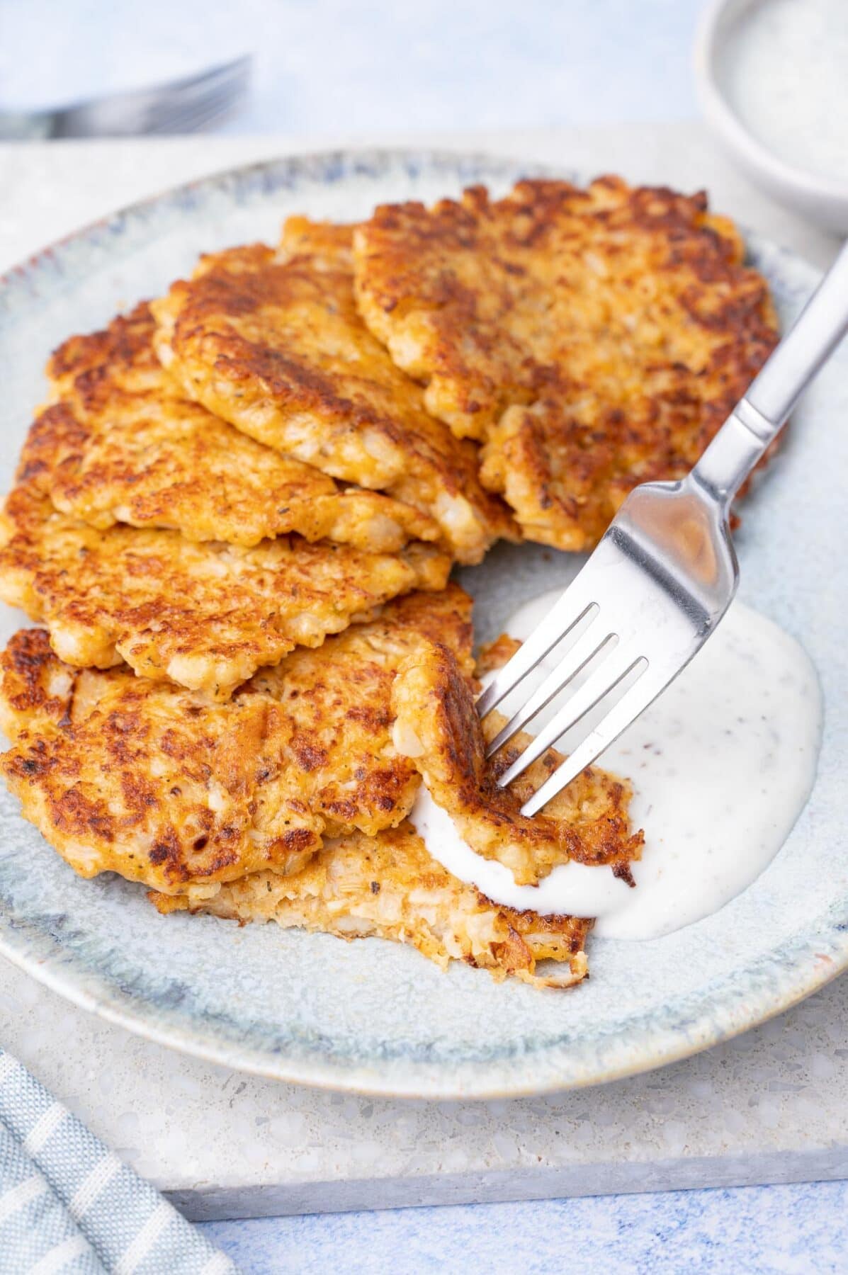 Cauliflower fritters on a blue plate are being dipped into yogurt dip.