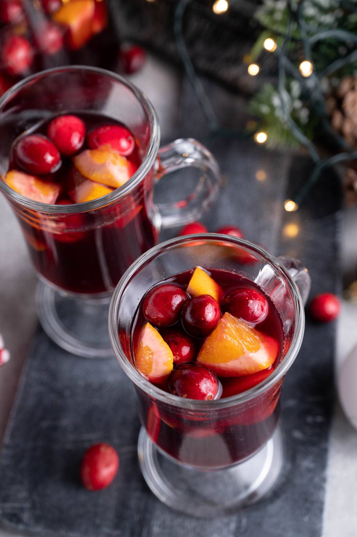 Two glasses with cranberry orange sangria on a black board.