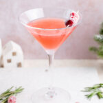 Cranberry martini in a martini glass decorated with sugared cranberries on a white stone board.