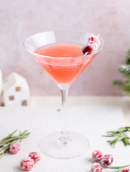 Cranberry martini in a martini glass decorated with sugared cranberries on a white stone board.