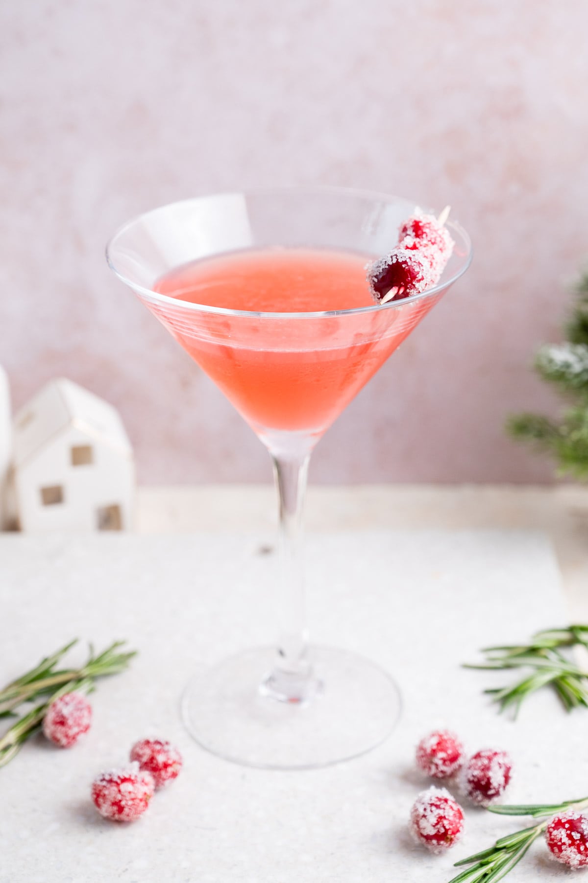 Cranberry martini in a martini glass decorated with sugared cranberries on a white stone board.