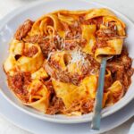 Duck ragu with pappardele pasta in a beige plate.