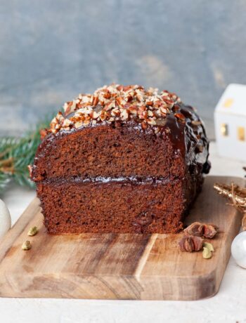 Piernik cake cut in half on a wooden board. Christmas decorations in the background.