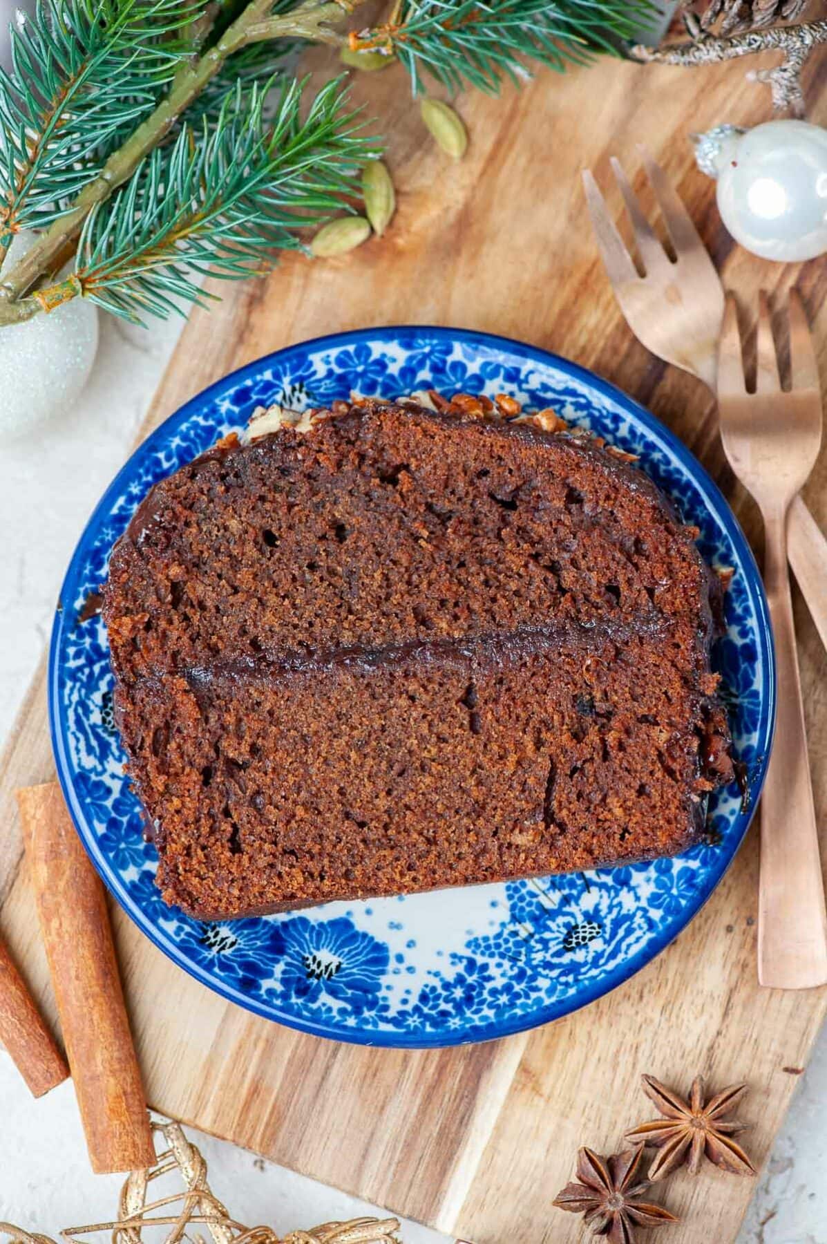 A slice of gingerbread cake on a blue plate.. Christmas decorations in the background.