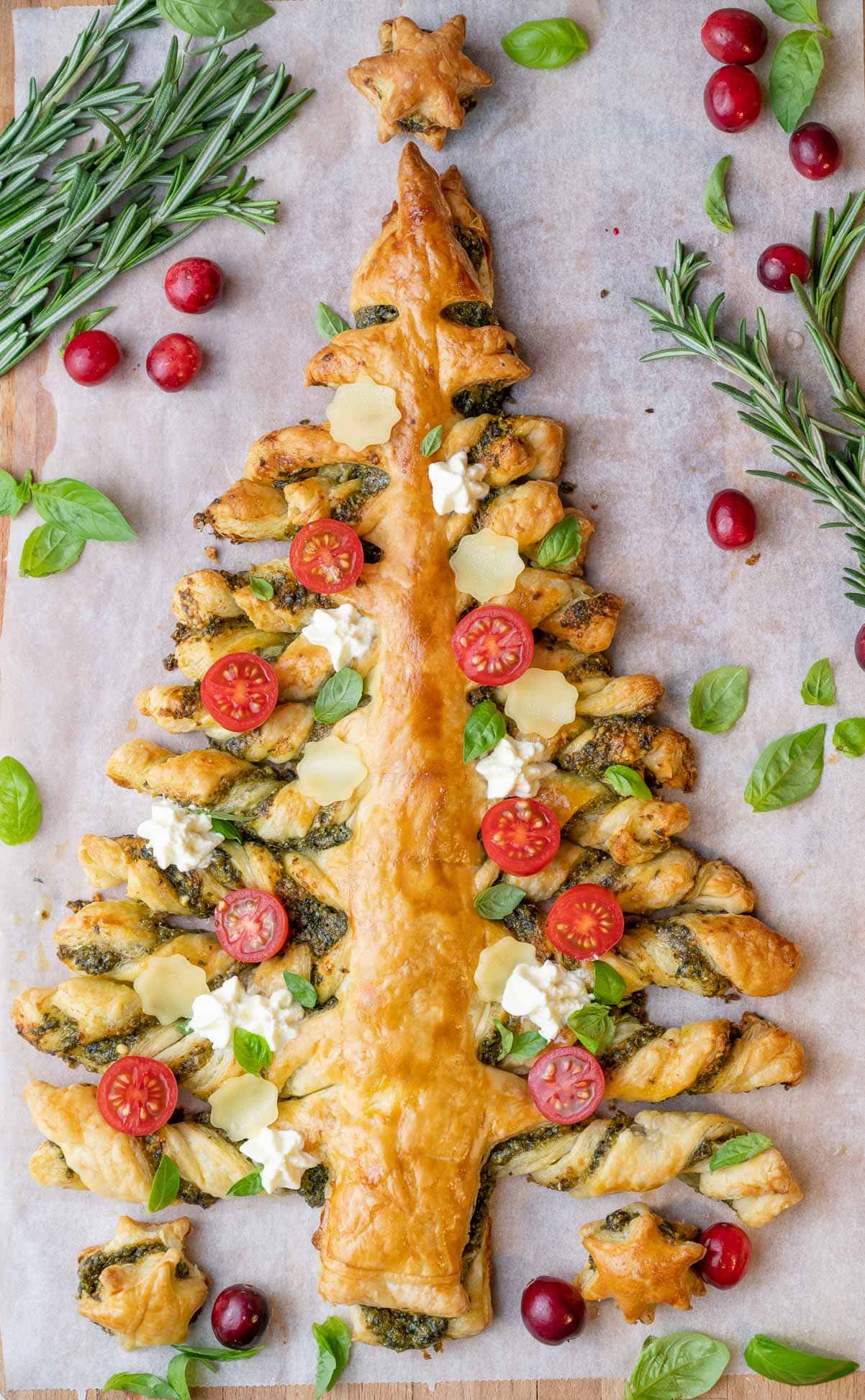 Puff pastry Christmas tree topped with tomatoes and basil on a piece of parchment paper.