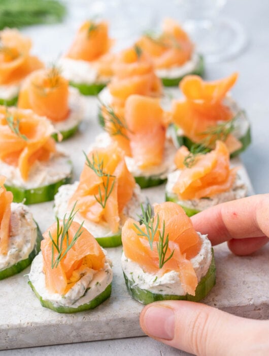 Smoked salmon appetizer with cucumbers and cream cheese on a stone board.
