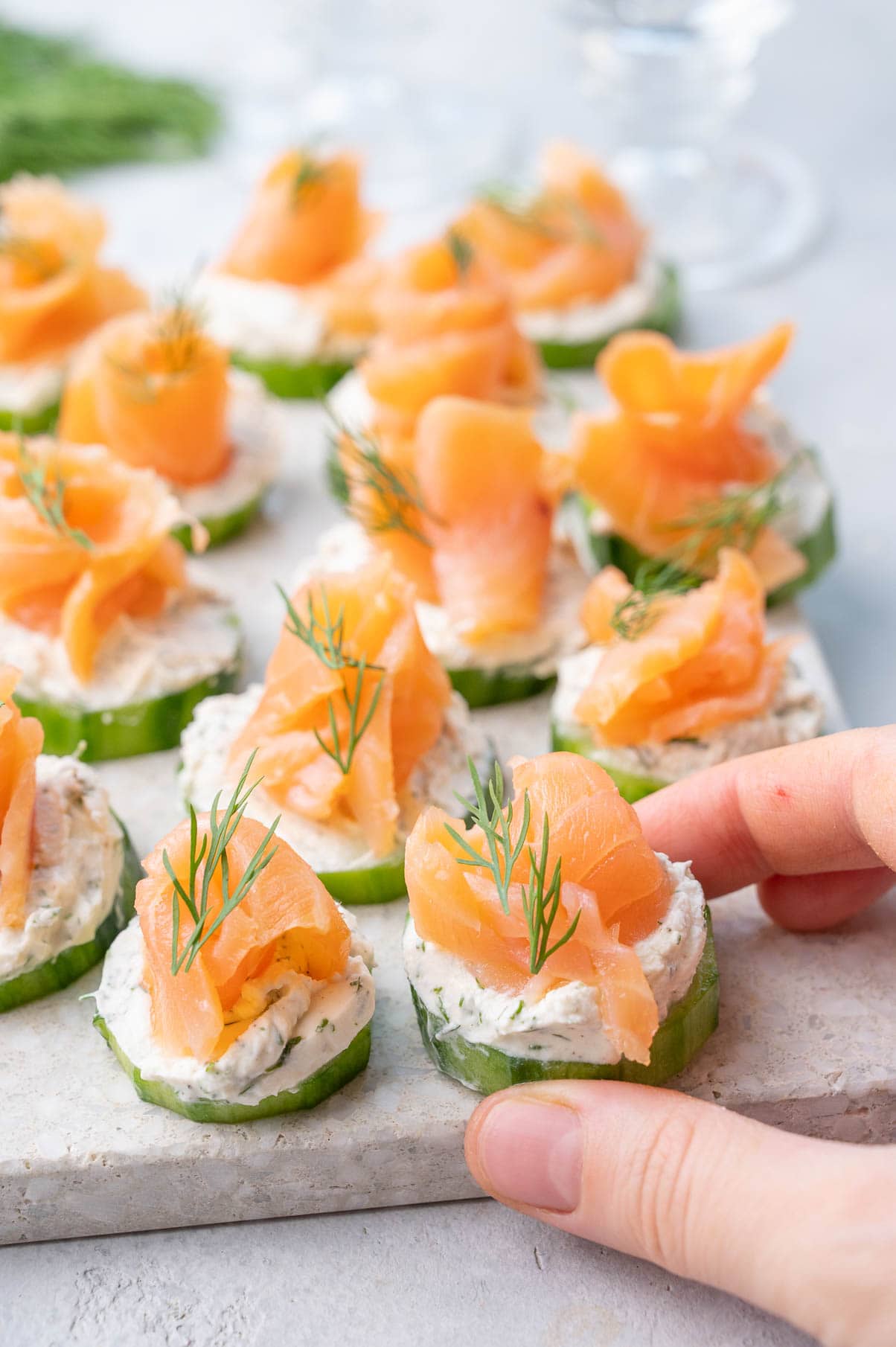 Smoked salmon appetizers held in a hand and on a white stone board.